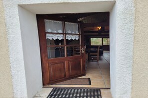 Une porte en bois ornée d’un rideau en dentelle, qui donne sur un espace extérieur aménagé avec une table et des chaises.
