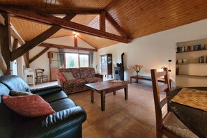A rustic interior with a wooden ceiling, a sofa, a coffee table, a bookshelf, and a fireplace. - Gîte with garden and shared pool (Saint-Saud-Lacoussière)