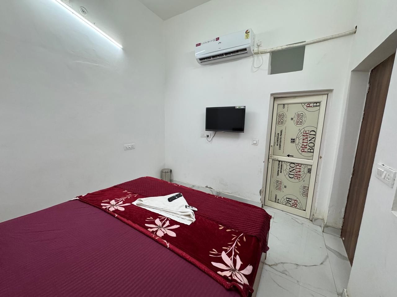 Une chambre dotée d’un lit simple, d’un appareil de climatisation, d’une télévision et d’une porte ornée d’un motif décoratif.