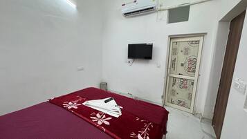 Une chambre dotée d’un lit simple, d’un appareil de climatisation, d’une télévision et d’une porte ornée d’un motif décoratif.