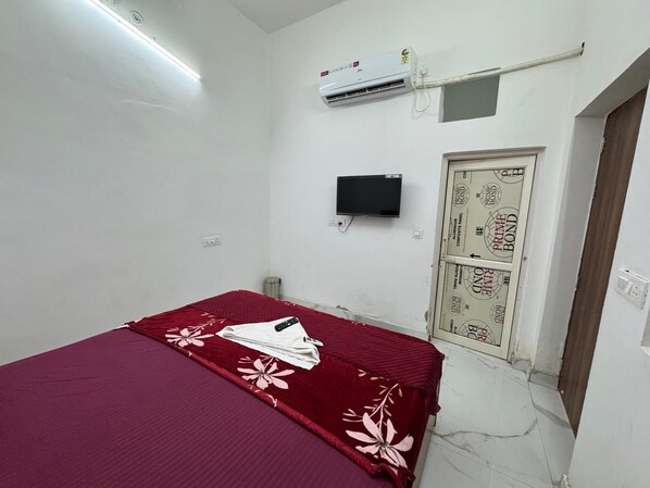 A bedroom with a single bed, an air conditioning unit, a television, and a door with a decorative design.
