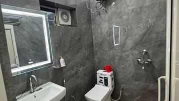 Une salle de bain moderne avec un lavabo blanc, un miroir et des toilettes, des murs en marbre et un seau rouge.