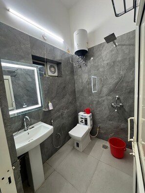 A modern bathroom with a white sink, mirror, and toilet, marble walls, and a red bucket.