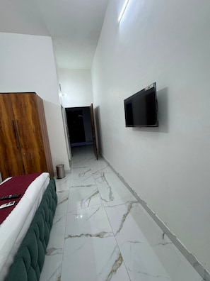 Habitación de hotel con cama, televisión montada en la pared y un pasillo que conduce a otra habitación.