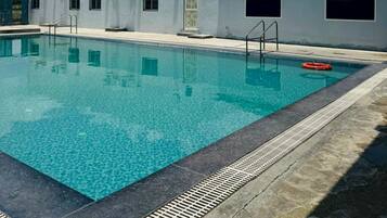 Une piscine à l’eau d’un bleu cristallin, entourée d’une terrasse en béton et bordée d’une rambarde de sécurité en métal.