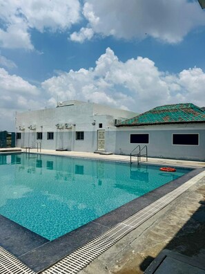 A swimming pool with clear blue water, surrounded by a concrete deck with a metal safety rail.