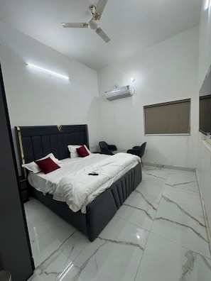 Un dormitorio con cama, mesitas de noche, ventilador de techo, aire acondicionado y una ventana.