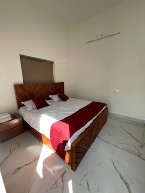 A bedroom with a bed, nightstand, and a headboard. - Manglaam Hotel & Resort (Greater Noida)