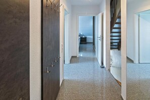 Un couloir avec une porte sombre, des murs blancs et un escalier menant à une autre pièce.