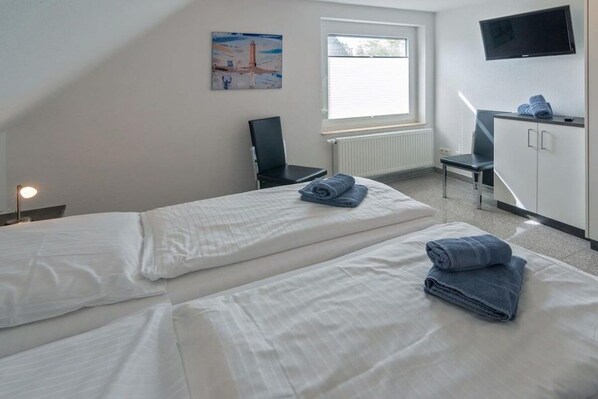 Quarto de hotel com duas camas, uma escrivaninha, uma cadeira, uma televisão e uma janela com persianas.