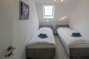 Ein kleiner, moderner Raum mit zwei Einzelbetten, einem Oberlicht und einem Bild an der Wand.