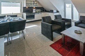 Cozinha moderna com armários brancos, micro-ondas e máquina de café. Há uma área de jantar com mesa e cadeiras, e um tapete vermelho no chão.