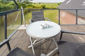Ein Balkon mit Tisch und Stühlen, der auf ein Gewässer und Grünflächen blickt.