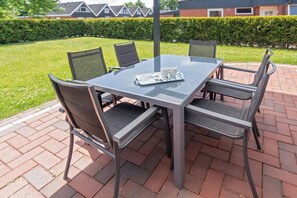 A glass-top table with four chairs, a tray with cups and a saucer, and a hedge in the background. - Holiday home with 2 bedrooms (Bensersiel)