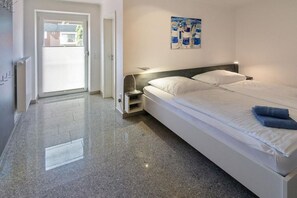 A hotel room with a bed, a nightstand, a door to the outside, and a wall with a painting. - Holiday home with 2 bedrooms (Bensersiel)