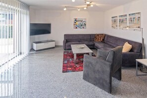 A modern living room with a grey sectional sofa, a coffee table, and a TV mounted on the wall. - Holiday home with 2 bedrooms (Bensersiel)