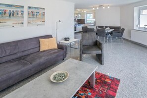 A modern living area with a sofa, coffee table, and a dining table with chairs. - Holiday home with 2 bedrooms (Bensersiel)