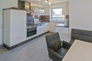 A modern kitchen with white cabinetry, a built-in oven, and a window providing natural light. - Holiday home with 2 bedrooms (Bensersiel)