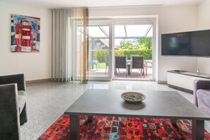 A modern living room with a flat-screen TV, a dining table with a bowl, and a colorful rug. - Holiday home with 2 bedrooms (Bensersiel)