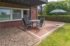 A patio with a table and chairs, a green umbrella, and a brick wall. - Holiday apartment with 1 bedroom (Bensersiel)