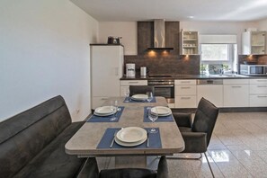 Cozinha moderna com área de jantar, incluindo uma mesa posta para quatro pessoas, um sofá e um forno embutido.