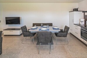 Cozinha moderna com mesa de jantar posta para quatro pessoas, televisão de tela plana na parede e cafeteira no balcão.