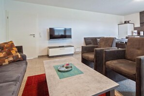 A modern living room with a flat-screen TV, a sofa, a coffee table, and a dining area with chairs. - Holiday apartment with 1 bedroom (Bensersiel)
