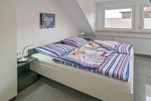 En enkeltseng med stribet sengetøj i et rum med skråvægge og et vindue.