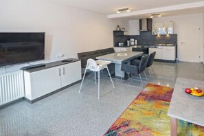 Et moderne køkken med spiseplads, et fladskærms-tv og et farverigt tæppe.