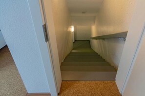 Un escalier recouvert de moquette, doté d’une main courante, menant à un palier éclairé par un luminaire.