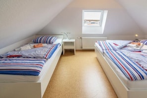 A small, triangular attic bedroom with two beds, a window, and a radiator. - Holiday home with 1 bedroom (Neuharlingersiel)