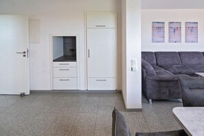 Een moderne woonkamer met een grijze bank, een eettafel en een keuken met kasten en een koelkast.