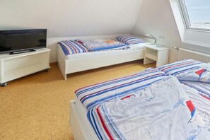 Een slaapkamer met een televisie op een dressoir, twee bedden met gestreepte lakens, een nachtkastje met een lamp en een raam met uitzicht.