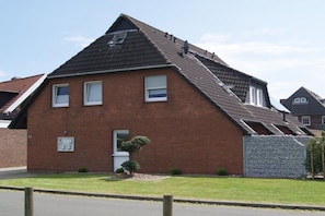 A two-story brick house with a sloped roof, a small front yard, and a visible satellite dish. - Holiday home with 1 bedroom (Neuharlingersiel)