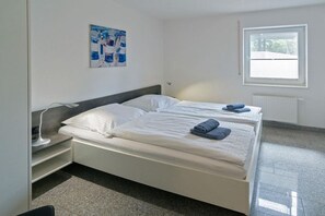 Une chambre à coucher avec un lit, une table de chevet, une lampe, une fenêtre et un radiateur.