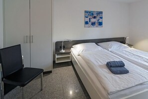 A hotel room with a bed, a chair, a nightstand, and a painting on the wall. - Holiday apartment with 2 bedrooms (Bensersiel)