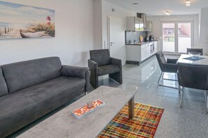 Ein modernes Wohnzimmer mit Sofa, Sessel, Couchtisch und einem farbenfrohen Teppich.
