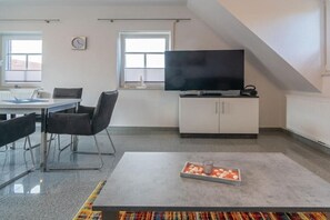 Ein modernes Wohnzimmer mit Flachbildfernseher, Essbereich mit Tisch und Stühlen und einem farbenfrohen Teppich.
