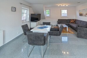 Ein modernes Wohnzimmer mit Flachbildfernseher, einem Esstisch mit Stühlen, einer Couch und einem Couchtisch.