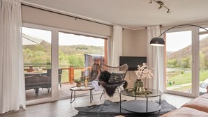 A spacious living room with a large window, a sofa, a coffee table, and a TV. - Holiday apartment Mila OG (Rieden)