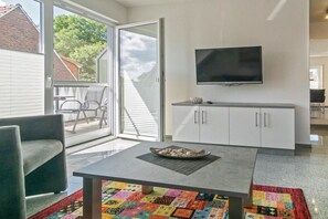 A modern living room with a flat-screen TV, a sofa, a coffee table with decorative items, and a colorful rug. - Holiday apartment with 1 bedroom (Bensersiel)