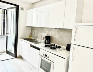 Una cocina moderna con armarios blancos, un lavamanos de acero inoxidable, una cafetera, un tostador y un horno empotrado.