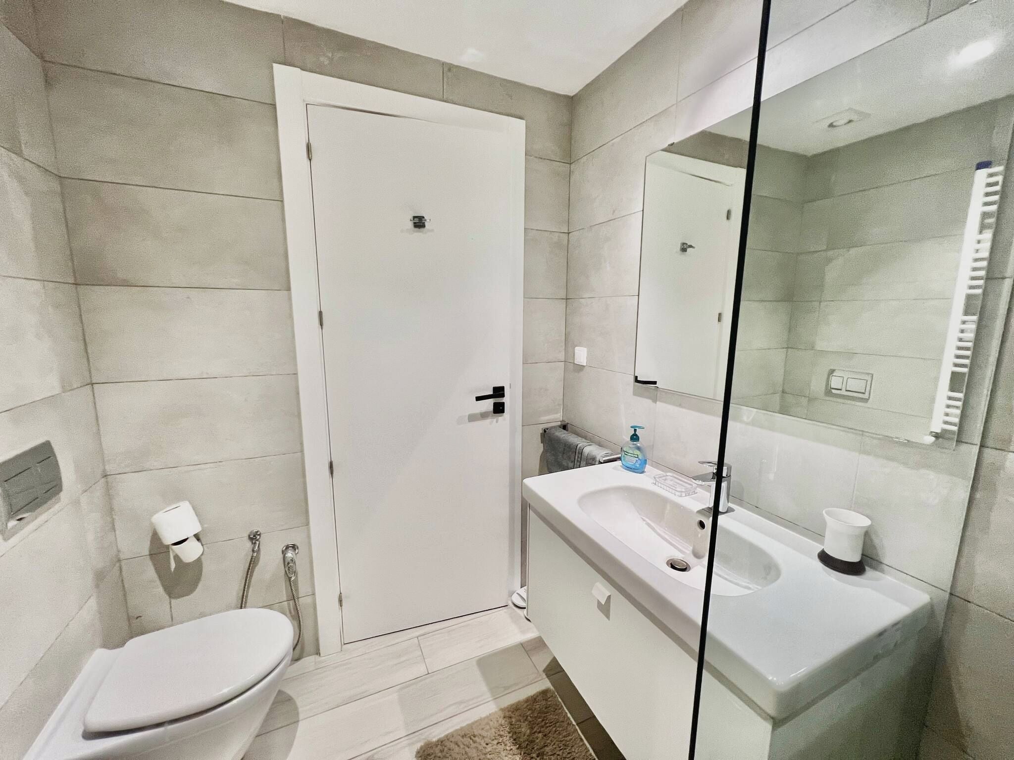 Een moderne badkamer met toilet, wastafel en een douchecabine met glazen wanden.