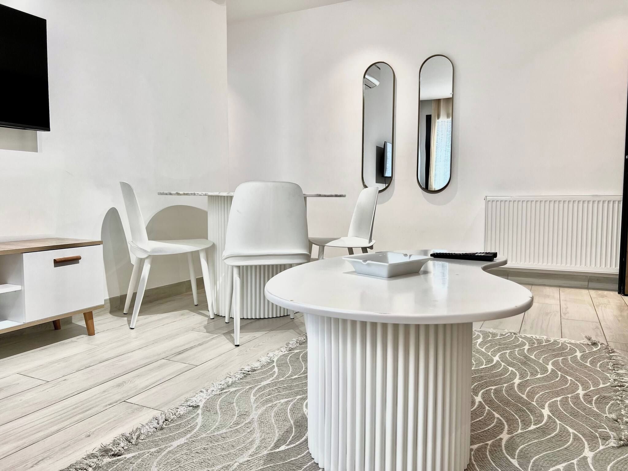 Une pièce moderne et minimaliste, avec une table ronde blanche, deux chaises blanches, un meuble blanc et un téléviseur fixé au mur.