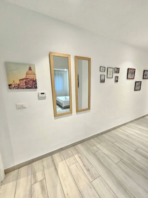 Habitación de hotel con cama, espejo montado en la pared, interruptor de luz e imagen enmarco de un edificio.