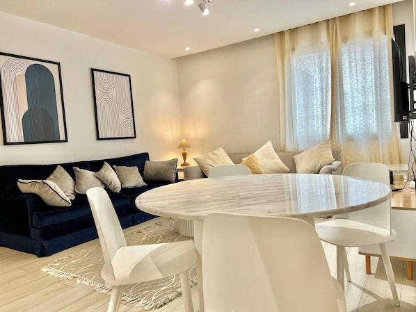 A modern living room with a dark blue sofa, white chairs, a round marble table, and two abstract paintings on the wall. - Luminous Escape to La Marsa (La Marsa)