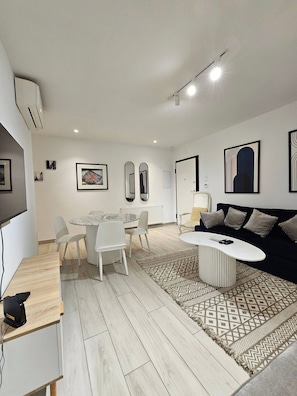 A modern living room with a round coffee table, a sofa, a dining table with chairs, and a TV mounted on the wall. - Luminous Escape to La Marsa (La Marsa)