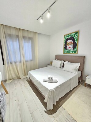 Una cama bien tendida con sábanas blancas, un cabecero y una obra de arte colgada en la pared.