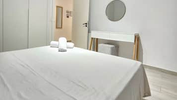 A modern bedroom with a large bed, a bedside table with a mirror, and a white wardrobe.