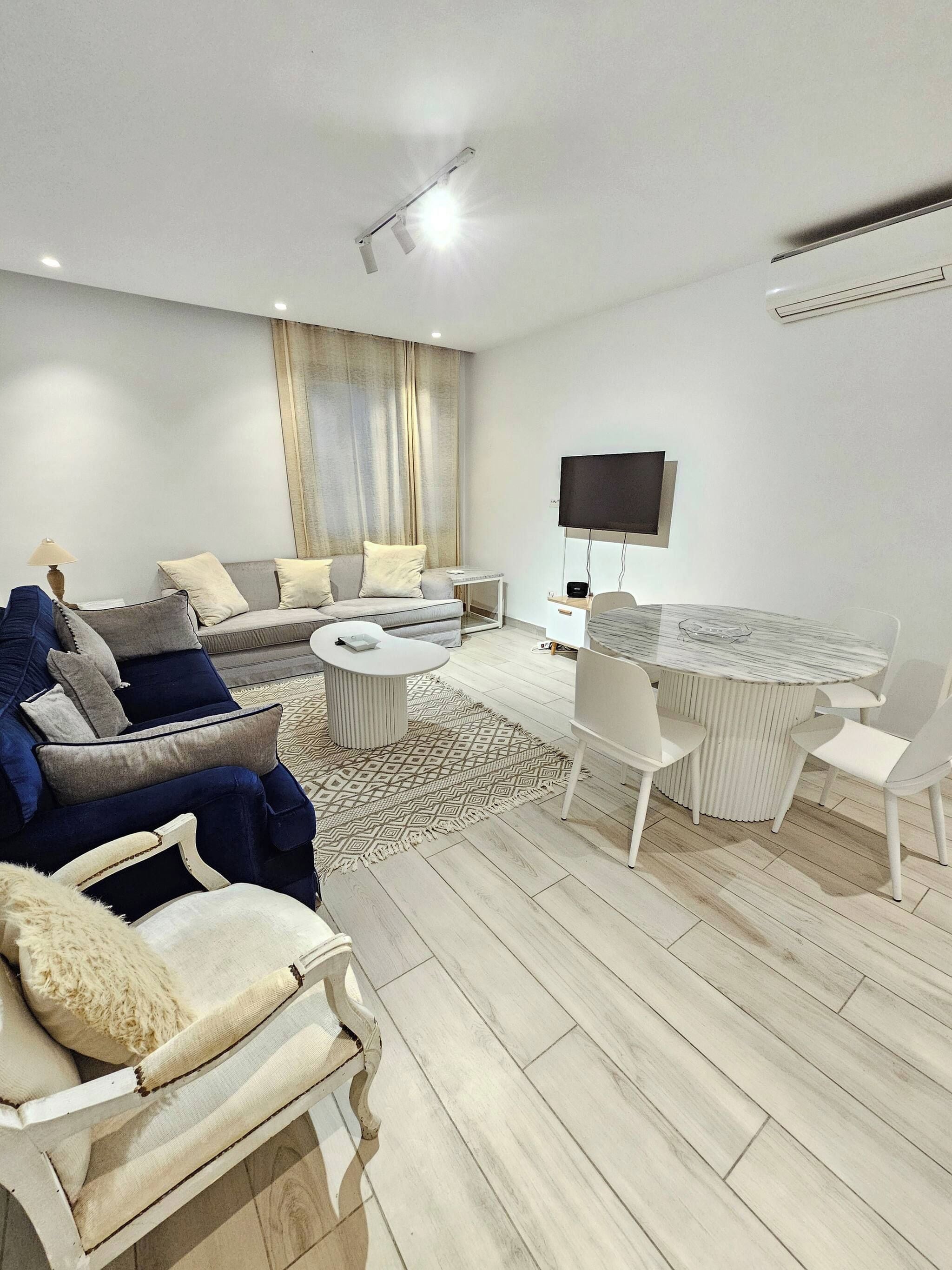 Una sala moderna con un sofá, sillones, una mesa de centro y una zona de comedor con una mesa y sillas.